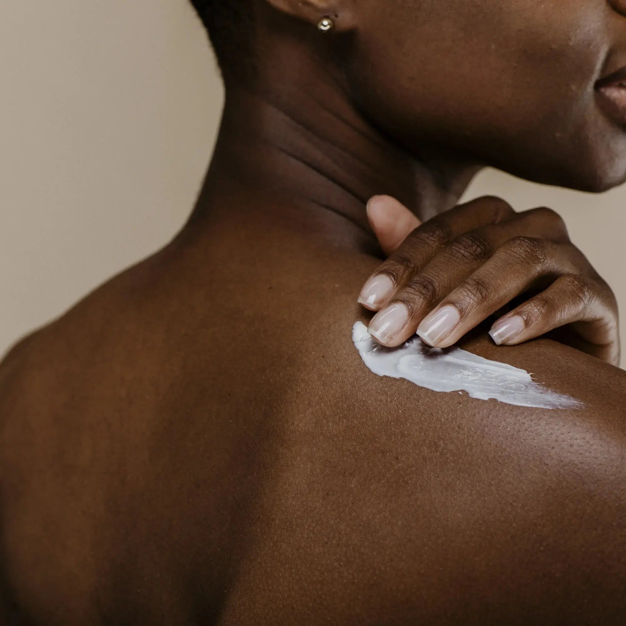 Femme appliquant la crème hydratante sur son épaule nue, geste doux de soin corporel