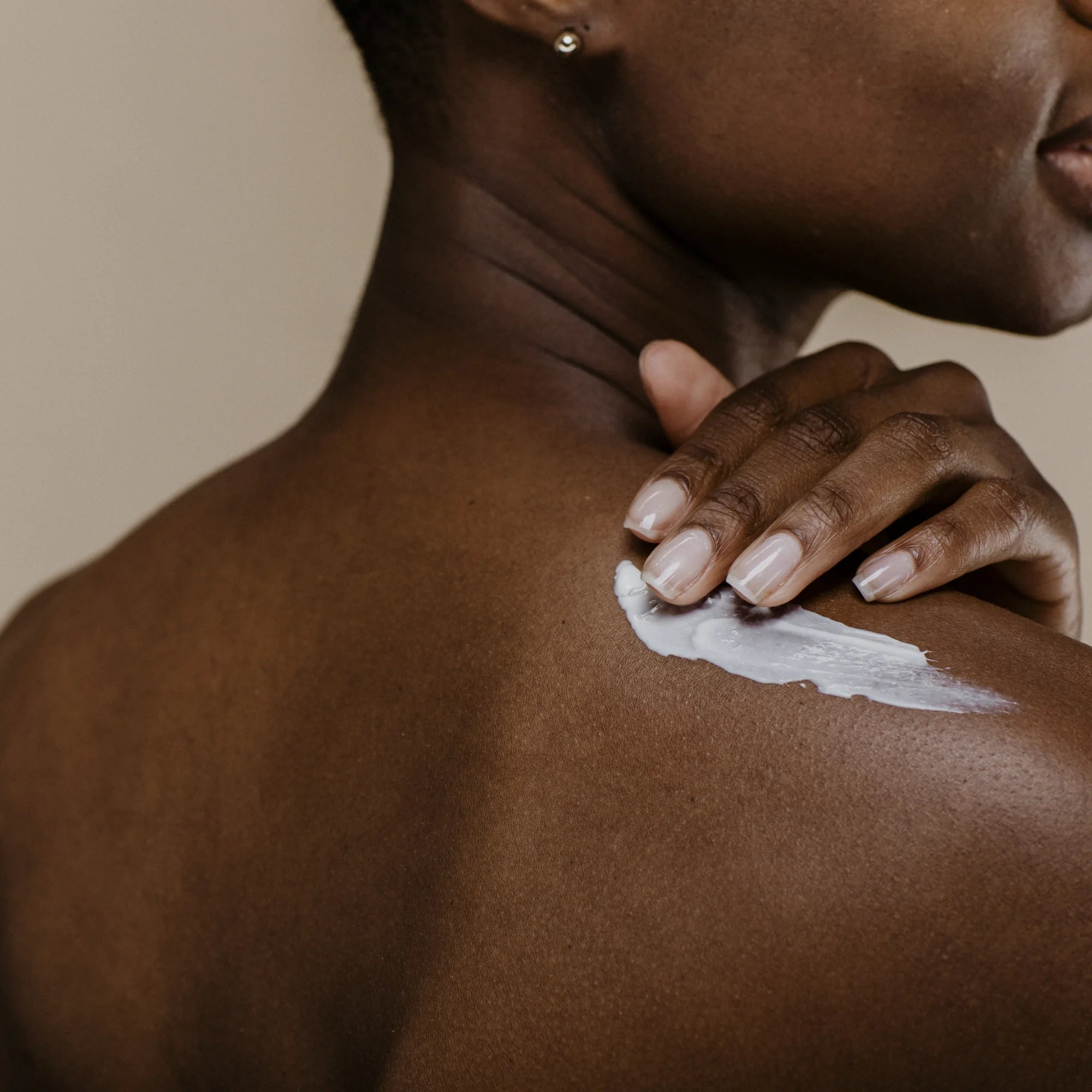 Femme appliquant la crème hydratante sur son épaule nue, geste doux de soin corporel