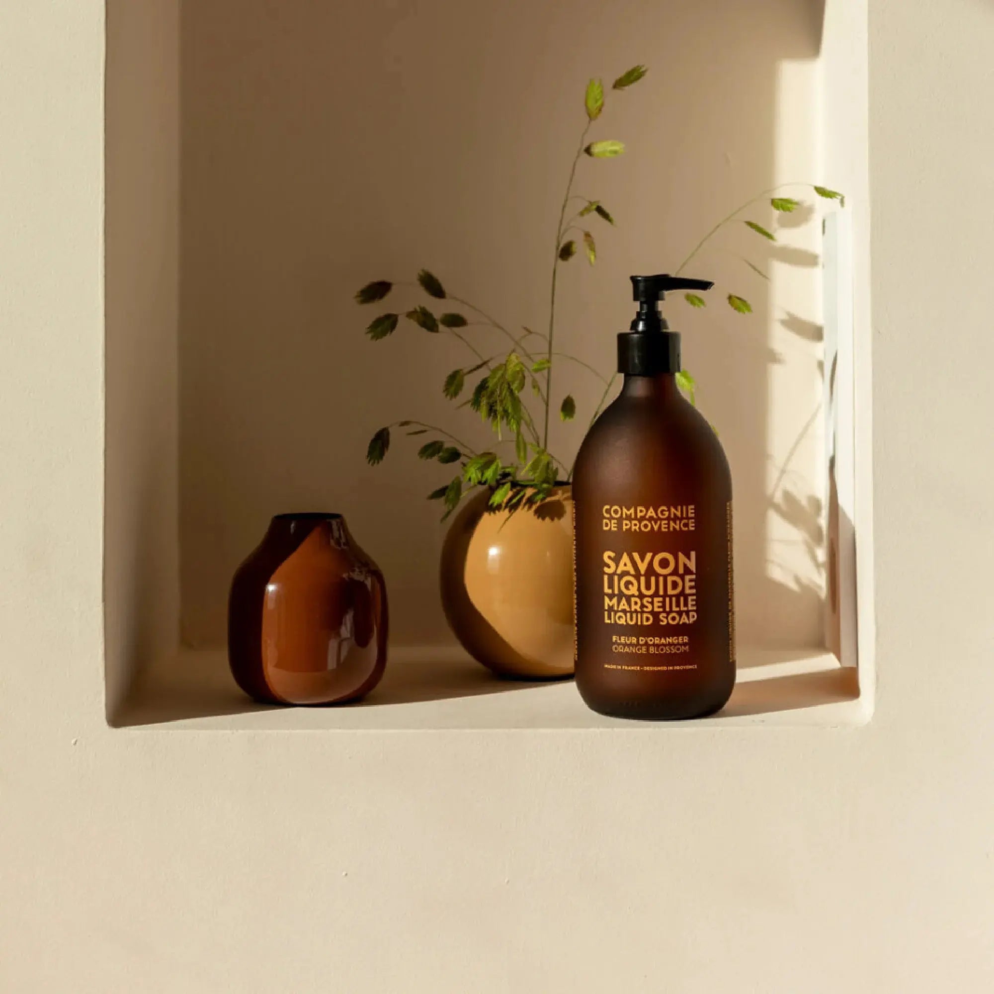 Savon liquide Fleur d'Oranger présenté dans une salle de bain lumineuse, posé près d'une plante et d'un autre flacon assorti.
