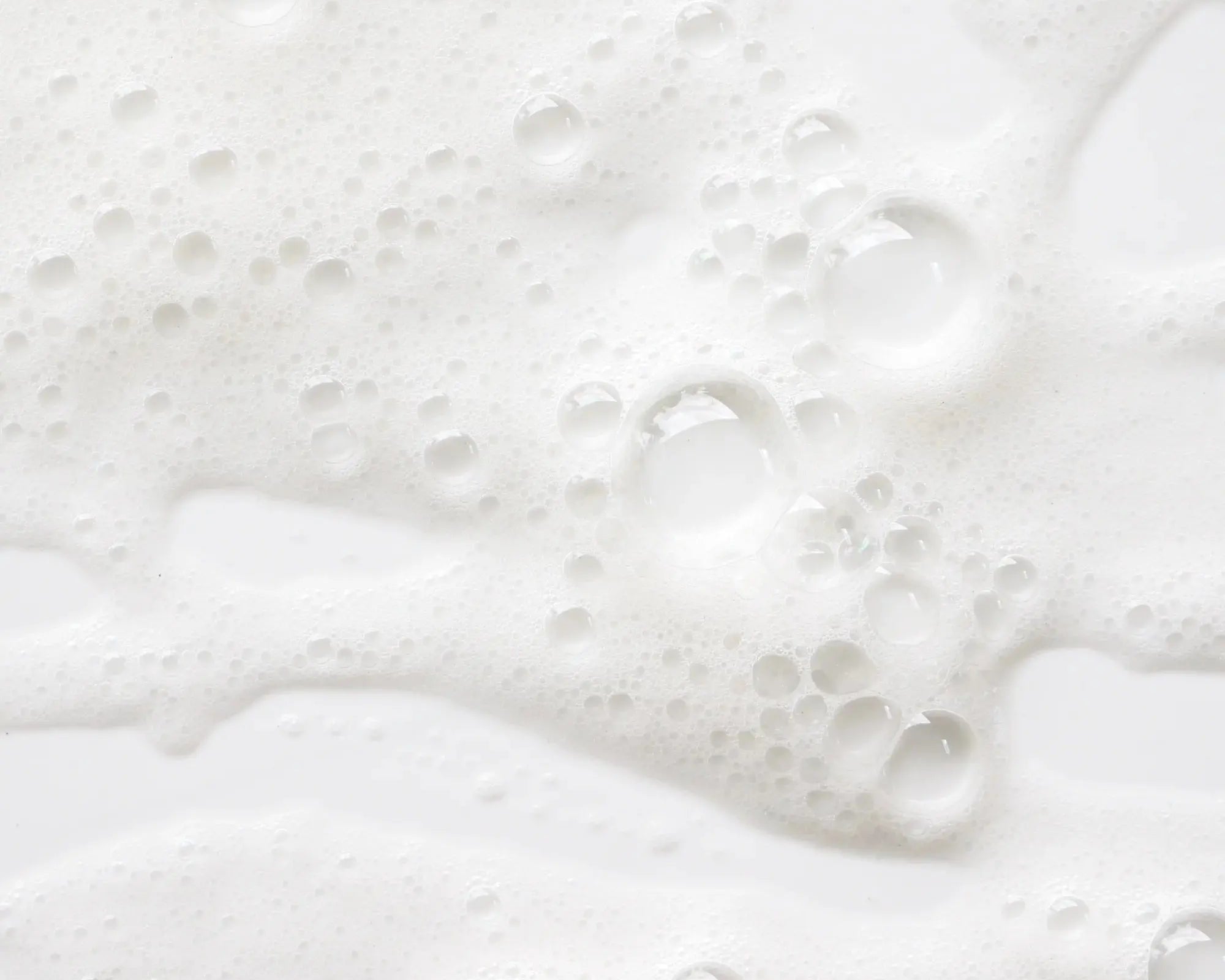 Zoom sur la mousse fine et aérienne du savon liquide Fleur d'Oranger, avec des bulles blanches sur fond clair
